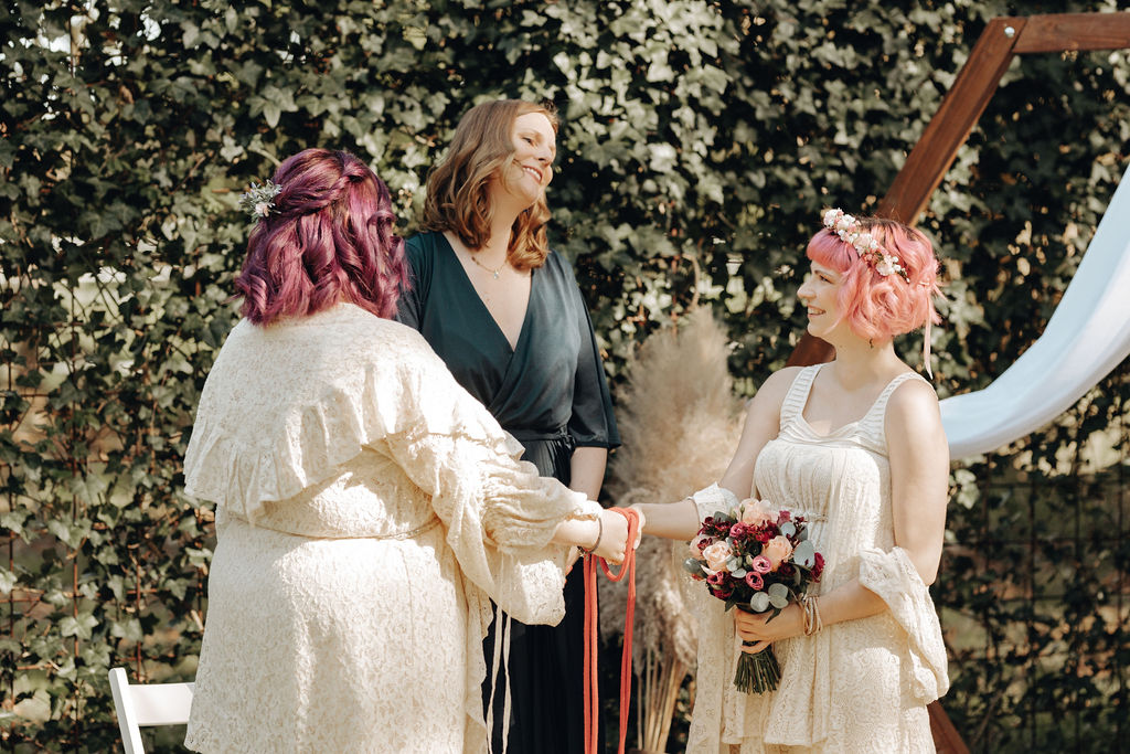 Freie Rednerin beim Handfasting Ritual mit zwei Bräuten mit pinkem Haar.